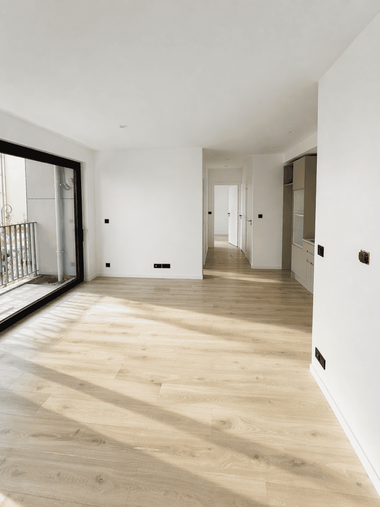 Appartement neuf avec parquet en bois clair et grande baie vitrée pour luminosité.