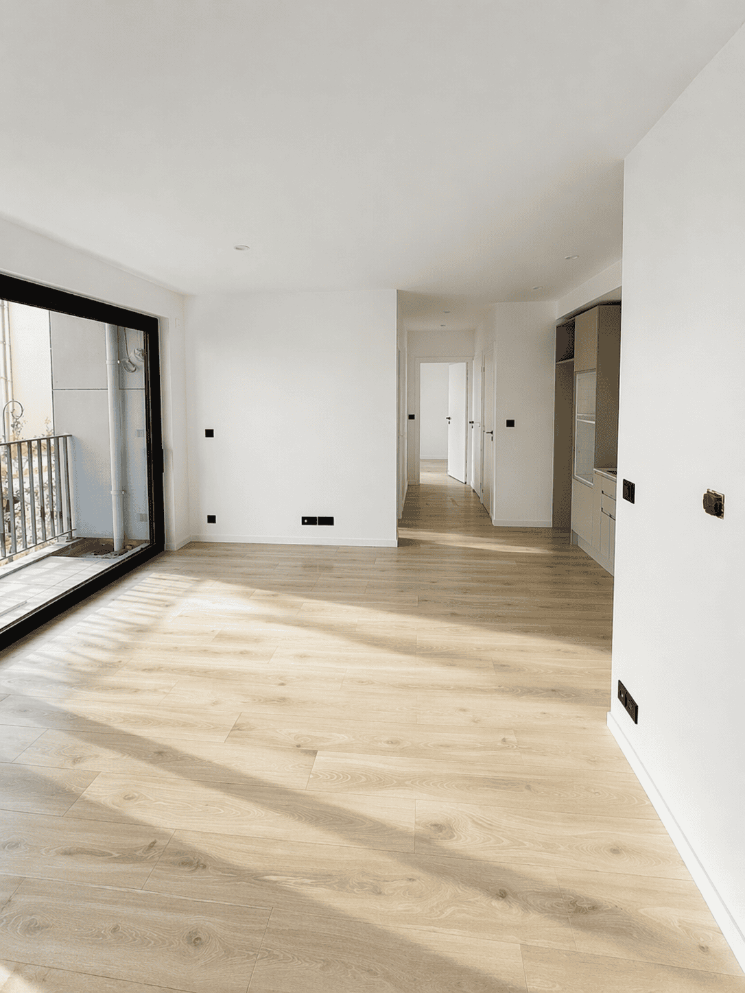 Appartement neuf avec parquet en bois clair et grande baie vitrée pour luminosité.