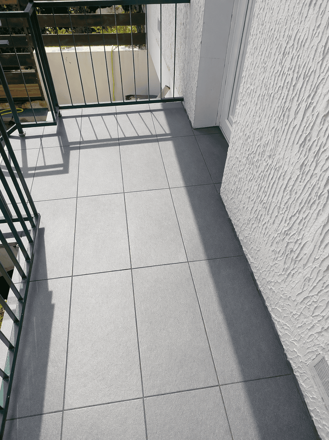 Balcon avec sol en pavés gris et barrière en métal noir.