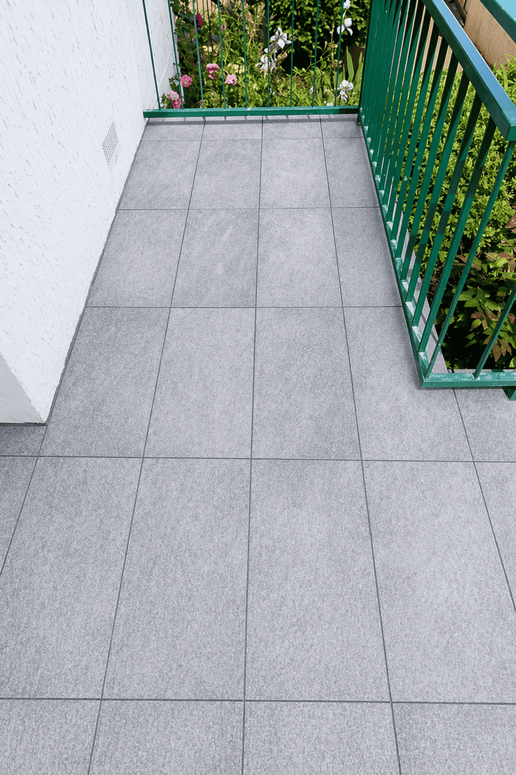 Balcon en carrelage gris avec garde-corps en métal vert, vue extérieure.