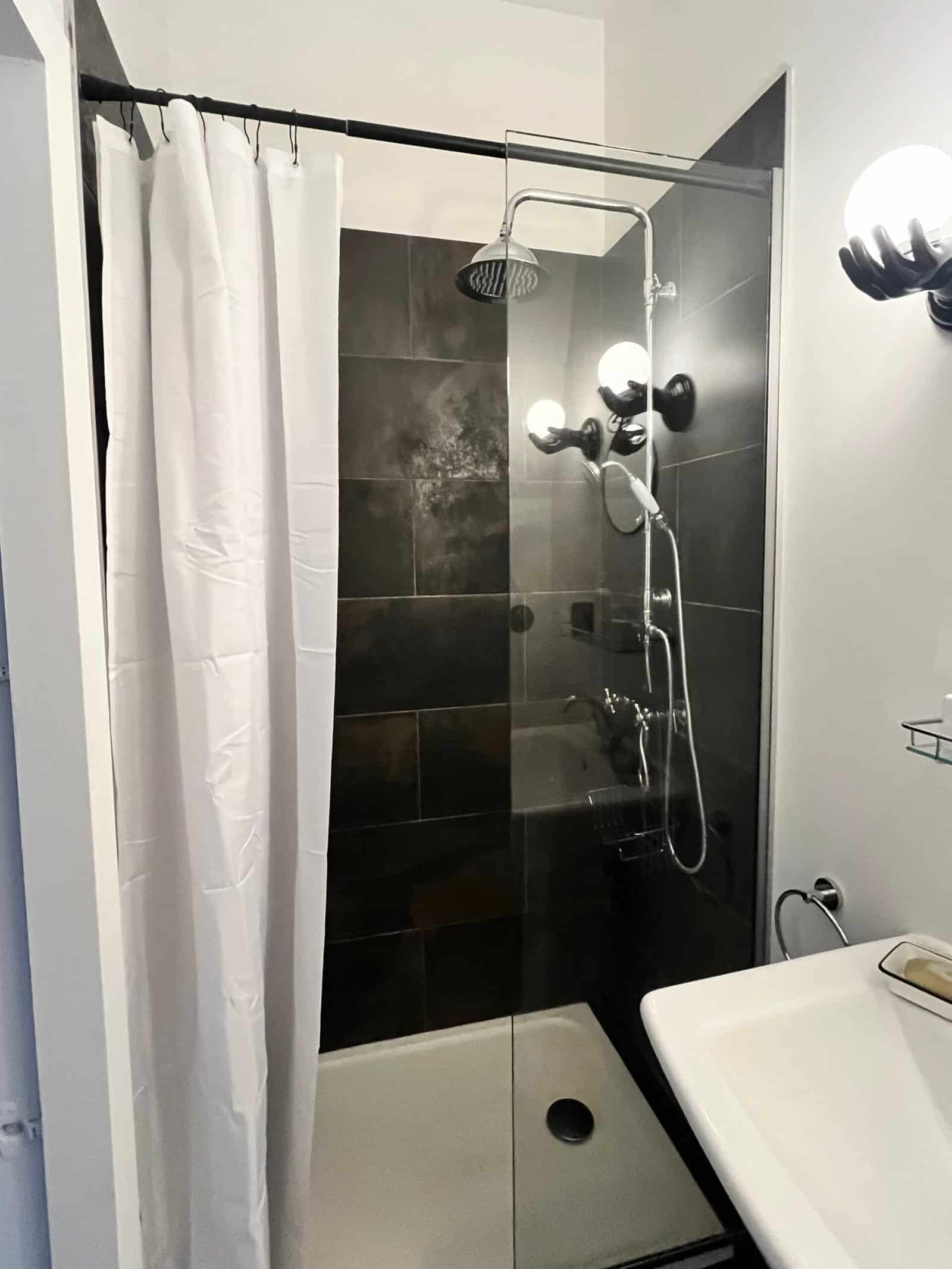 Salle de bain moderne avec douche à l'italienne, carrelage noir et éclairage élégant.